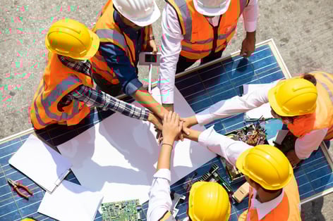 Construction workers huddle outdoors with hands in the center of team huddle