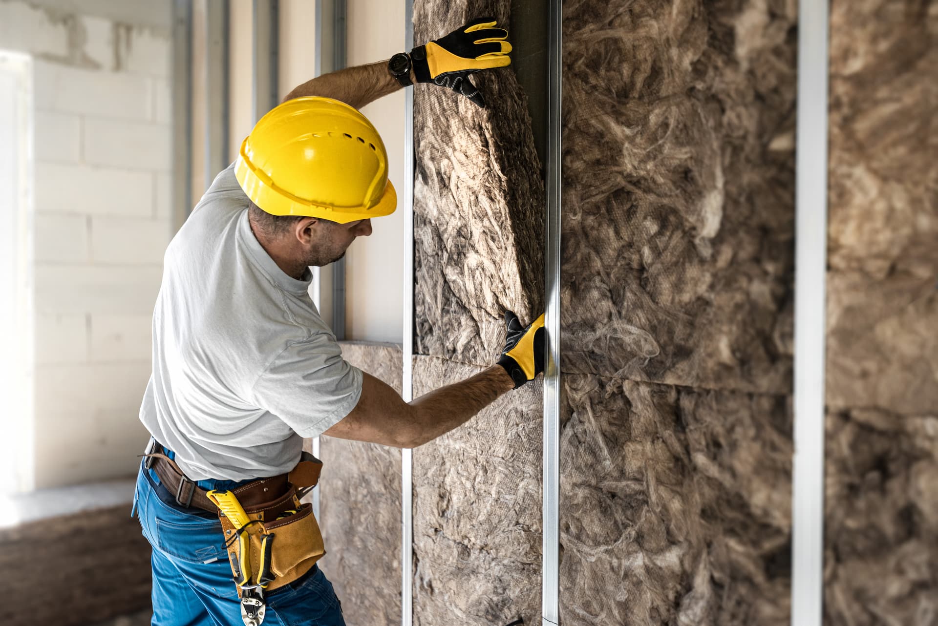 Subcontractor in yellow hardhat installing wall insulation